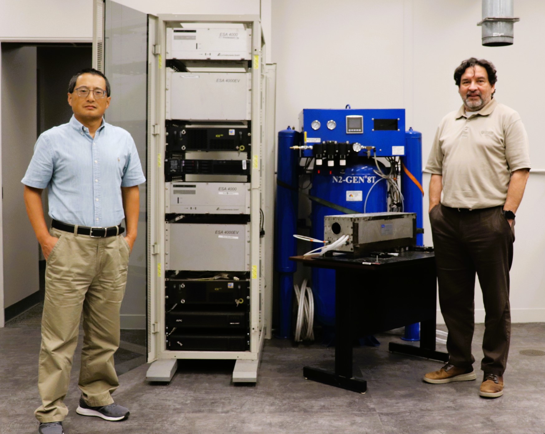 Zhen and Romero stand next to the cabinet, laser, and fuel source for their ML-Enhanced LIBS.